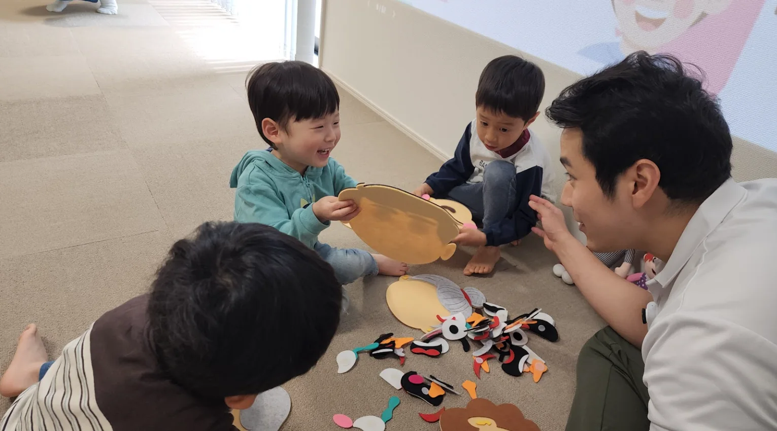 先生が子どもたちと小グループでやり取りしながら、低いプレッシャーの中で英語活動をしている様子